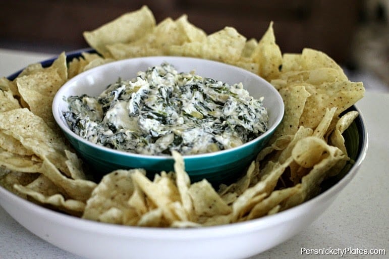 large bowl of tortilla chips surrounding a small bowl of spinach artichoke dip