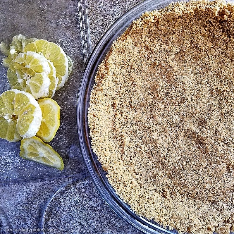 overhead shot of a graham cracker crust in a pie plate next to a pile of lemons.
