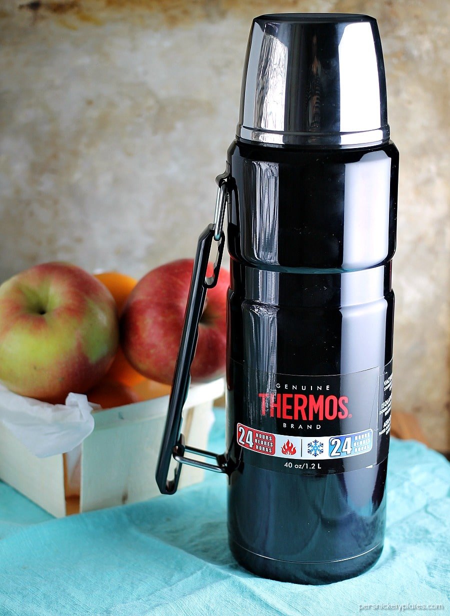 a black thermos in front of a basket of apples.