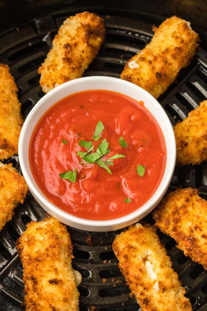 overhead shot of cheese sticks in an air fryer with a bowl of marinara.