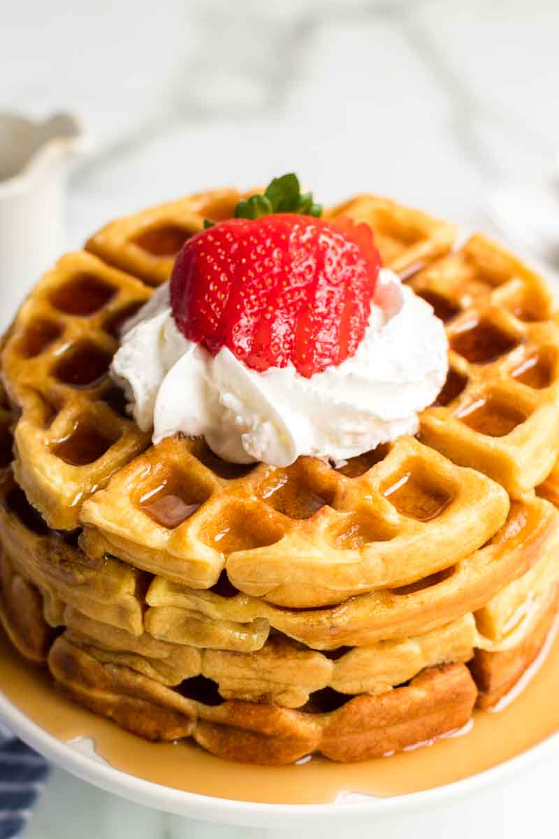 stack of 4 buttermilk waffles topped with syrup, whipped cream, and strawberries 