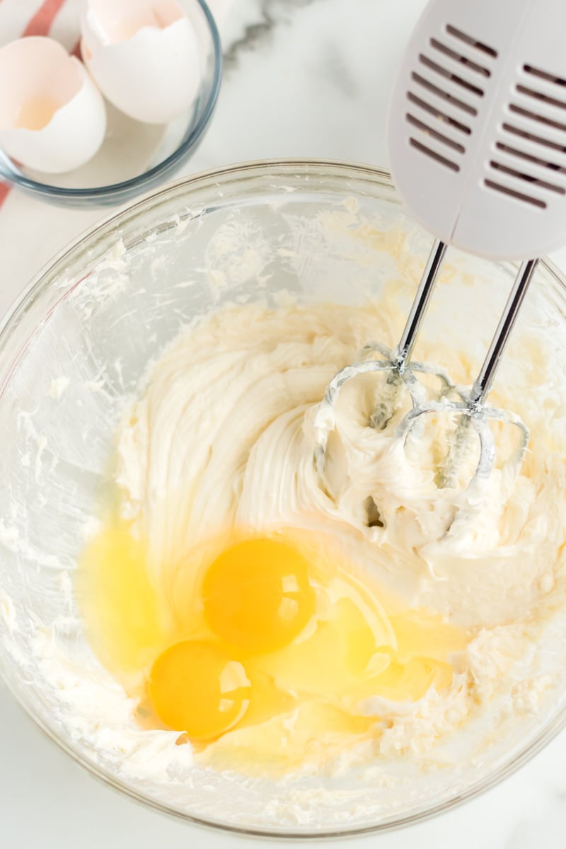 cheesecake batter in mixing bowl with cracked eggs.