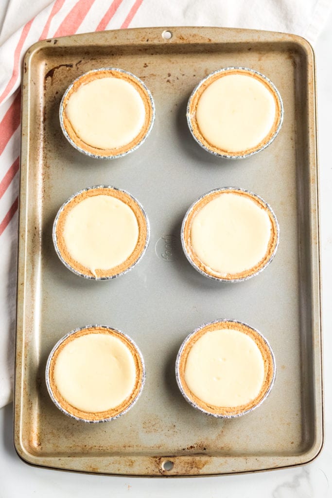6 mini cheesecakes on a baking sheet.