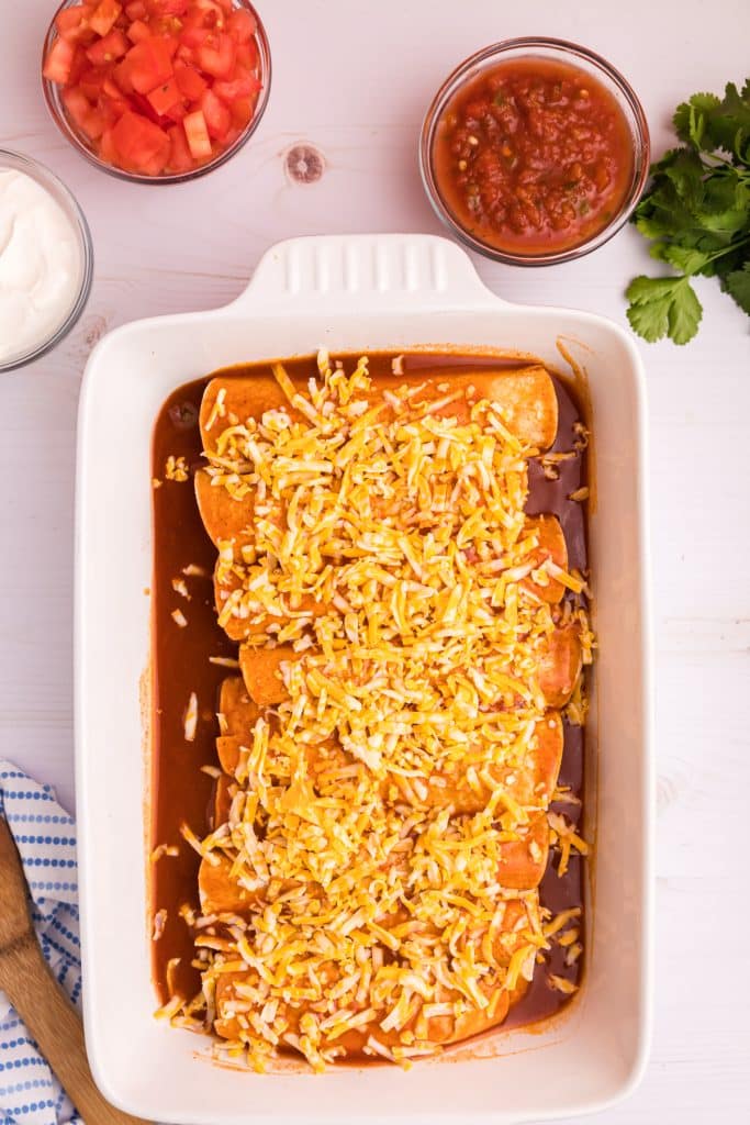 enchiladas topped with shredded cheese in a baking dish.