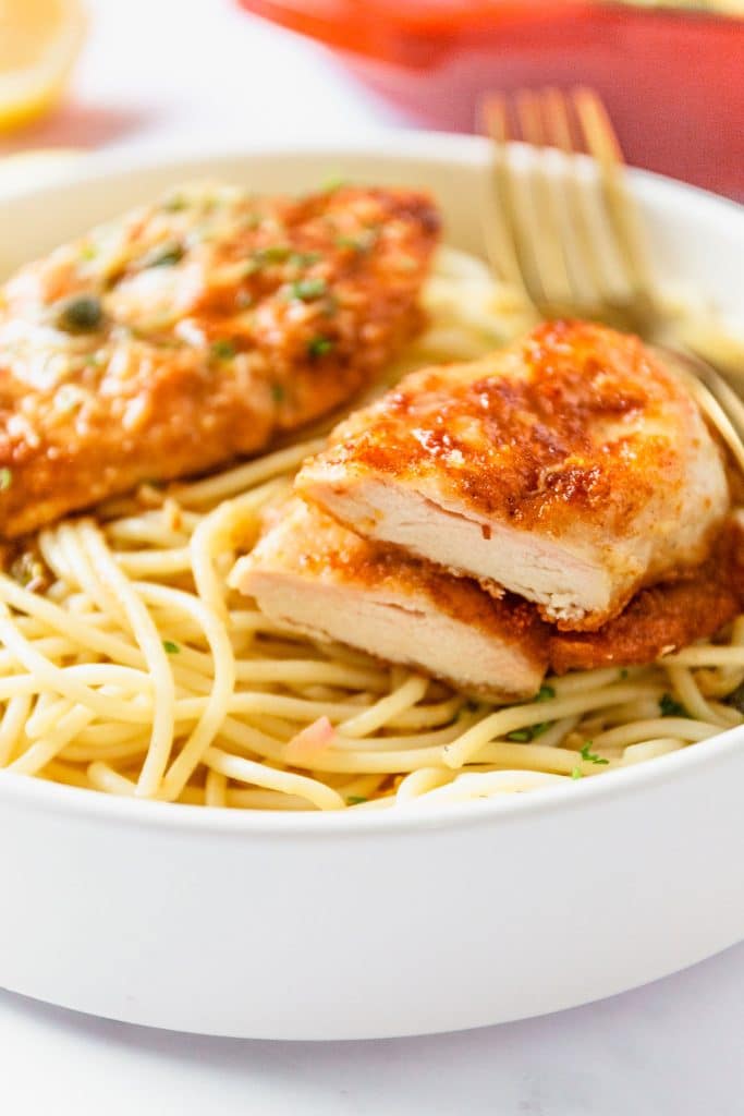 sliced chicken piccata breast stacked on a bed of noodles.