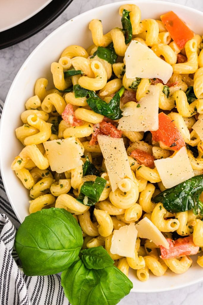 bowl of pesto cavatappi topped with shaved cheese, tomatoes, and spinach.