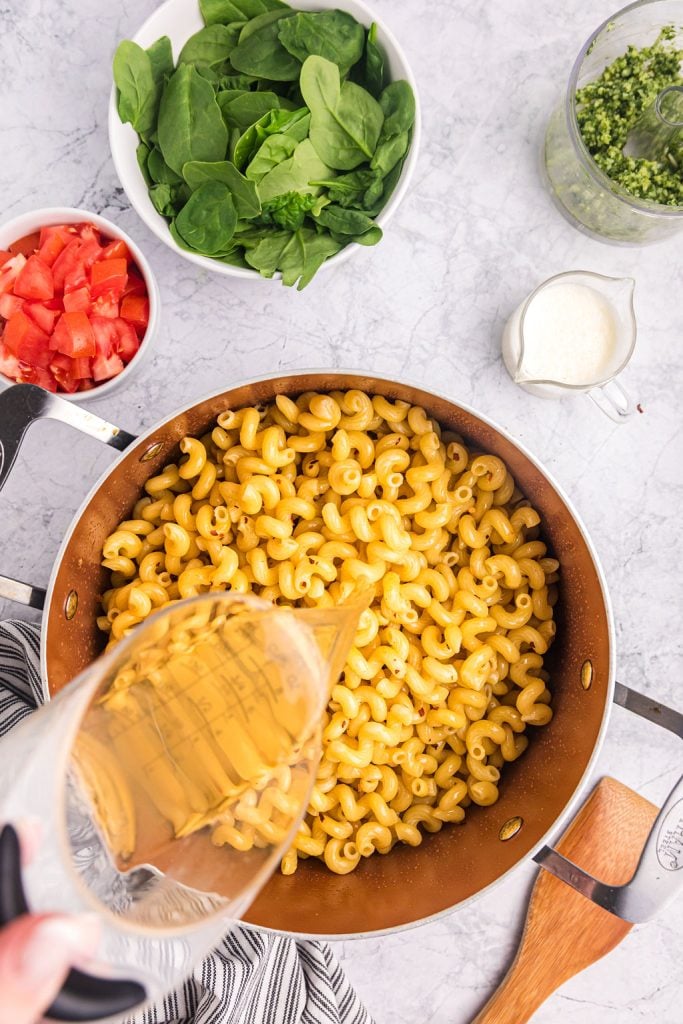 chicken broth pouring into a pot of cavatappi noodles.