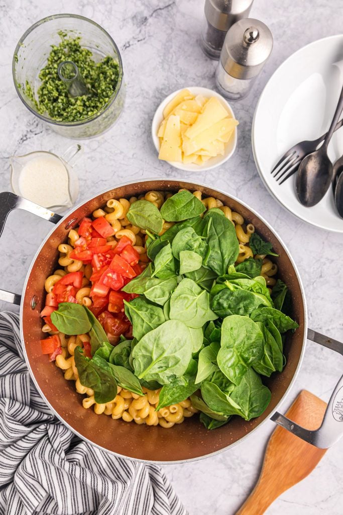overhead shot of fresh spinach and tomatoes in a pot of noodles.