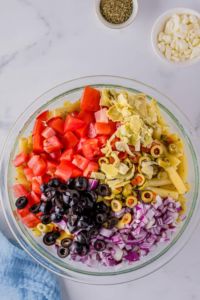overhead shot of olives, tomatoes, onions, and pasta in a glass bowl.