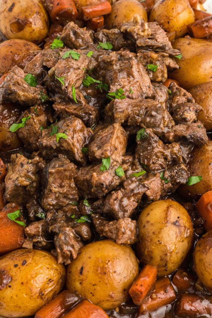 closeup of beef, potatoes, and carrots on a platter topped with parsley.