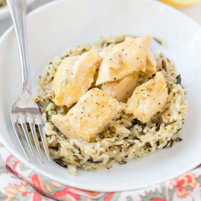 lemon chicken on a bed of rice in a white bowl with a fork