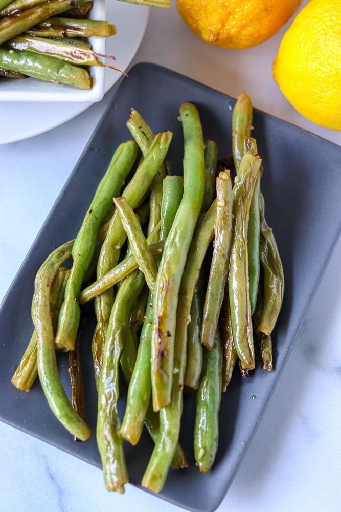 garlic green beans on grey platter with lemons in background 