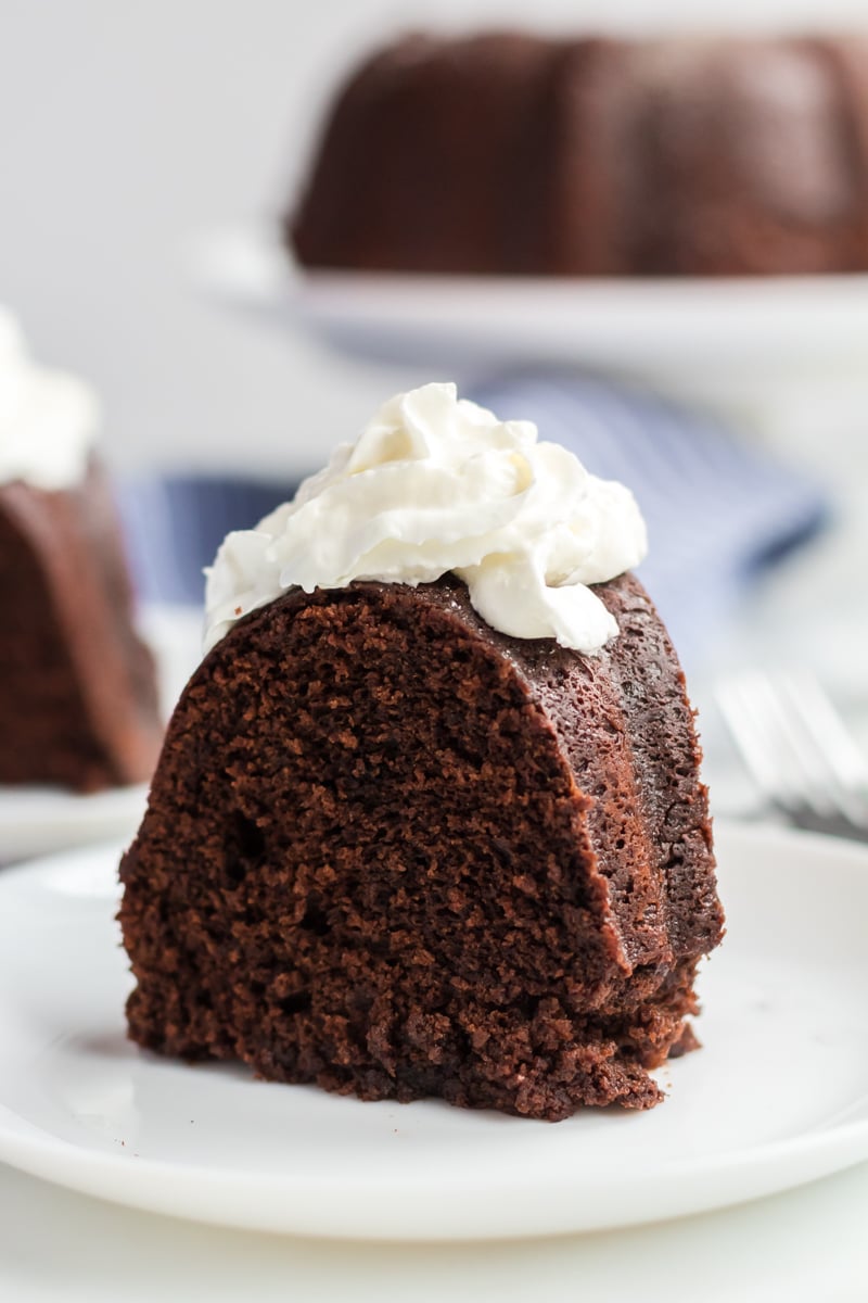 single slice of sour cream chocolate bundt cake on white plate topped with whipped cream 