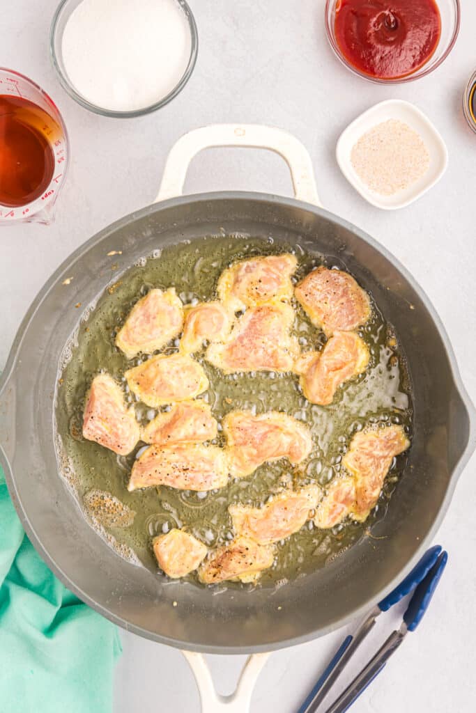 chicken pieces frying in a skillet.