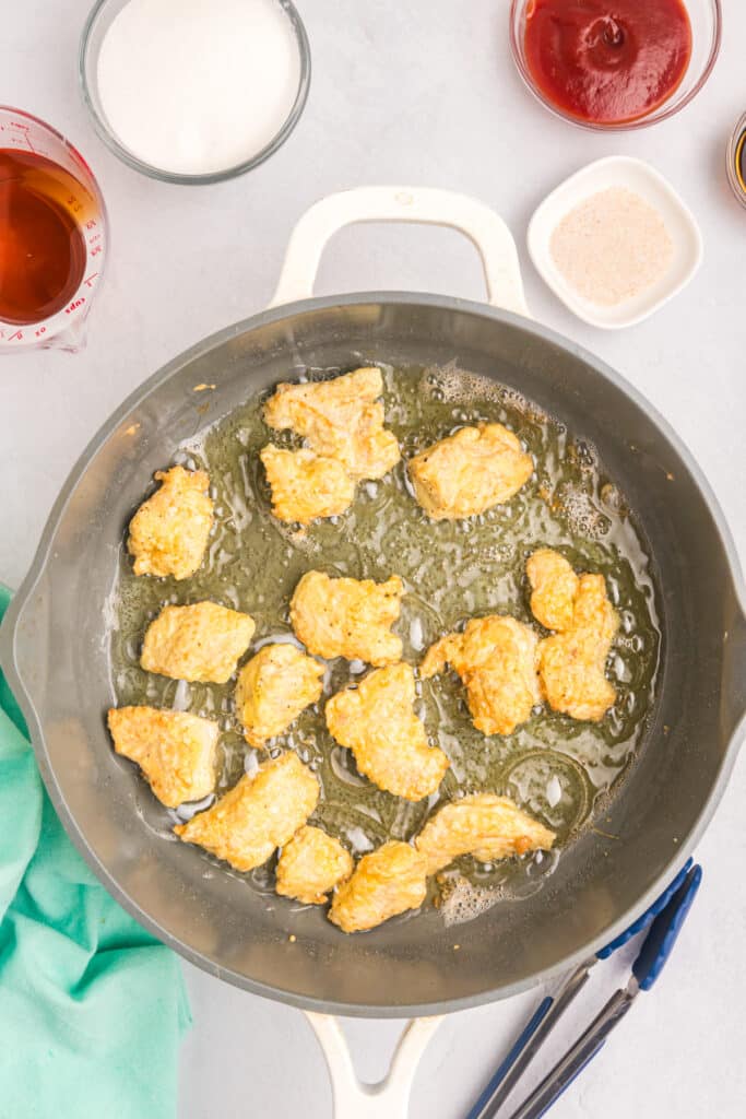 chicken chunks frying in oil in a skillet.