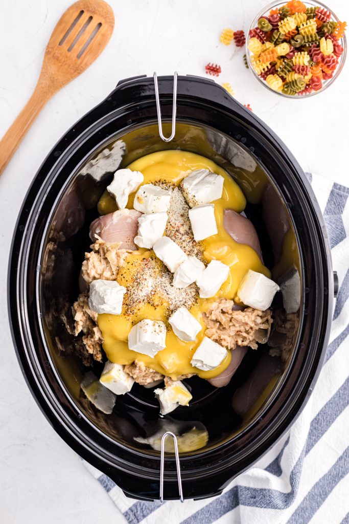 overhead shot of chicken and cubed cream cheese in a slow cooker.