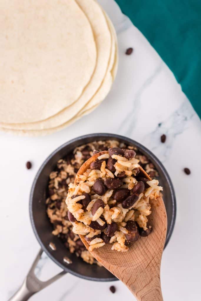 wooden spoon with a scoop of black beans & rice lifting from a pan.