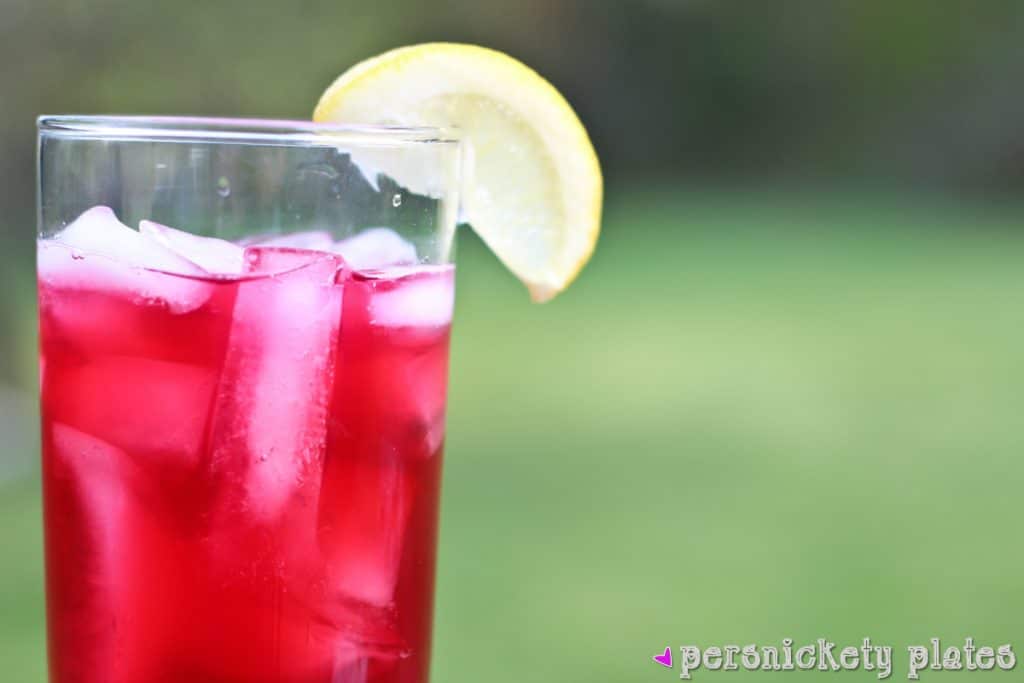 glass of pink passion tea lemonade with a lemon wedge.