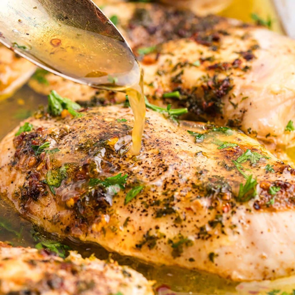 baked chicken breast with garlic butter being spooned over top.