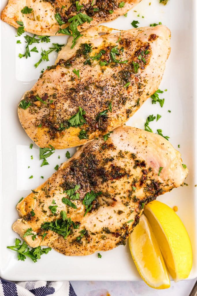 overhead shot of baked chicken on a white platter with lemon wedges.
