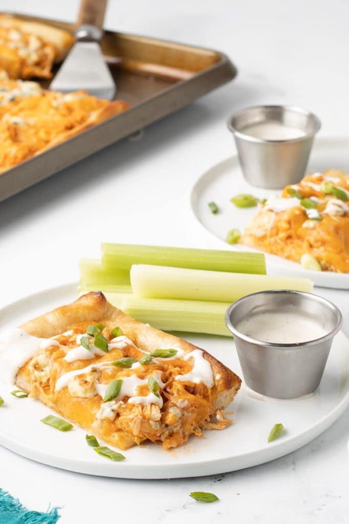slice of buffalo chicken pizza on a white plate with celery sticks.