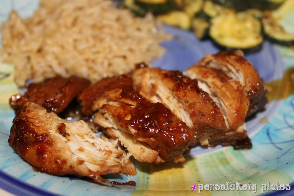 crockpot bourbon chicken sliced on a plate with brown rice and roasted zucchini.