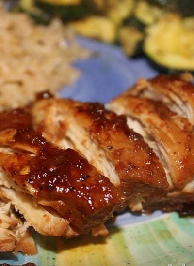 sliced honey bourbon chicken on a plate with rice and zucchini.