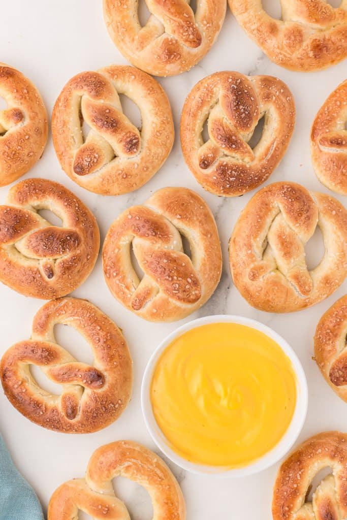 several homemade soft pretzels surrounding a bowl of cheese sauce.