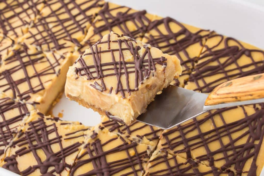 peanut butter cheesecake bar being lifted from a pan.