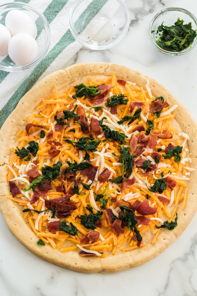 cheese, spinach, and bacon sprinkled on a pizza crust