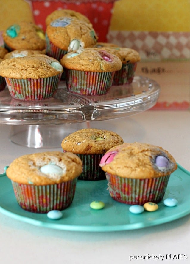 peanut butter m&m muffins on a teal plate in front of a serving platter of more muffins.