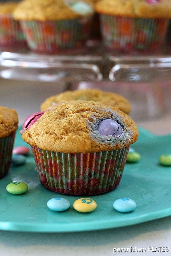 a muffin filled with colorful M&Ms and surrounded by additional M&Ms on a teal plate.