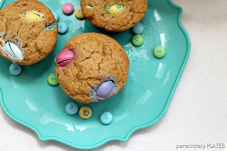 overhead shot of muffins filled with pastel colored M&Ms on a teal plate.