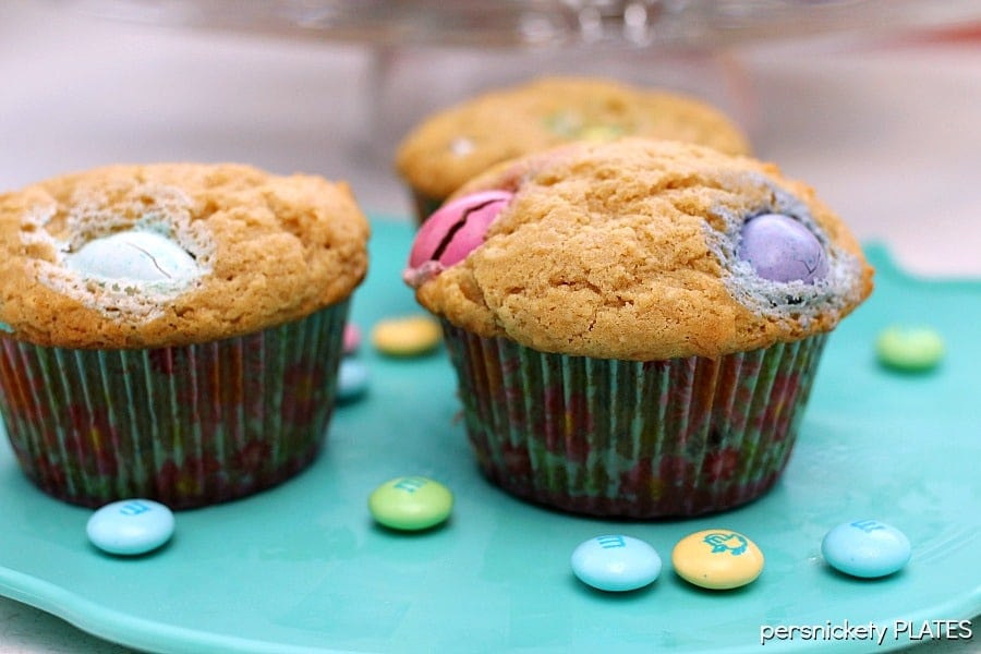 three muffins filled with pastel colored M&Ms on a teal plate.