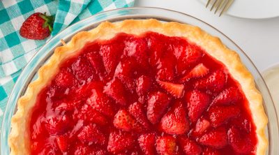 overhead shot of a fresh strawberry pie next to two gold forks.