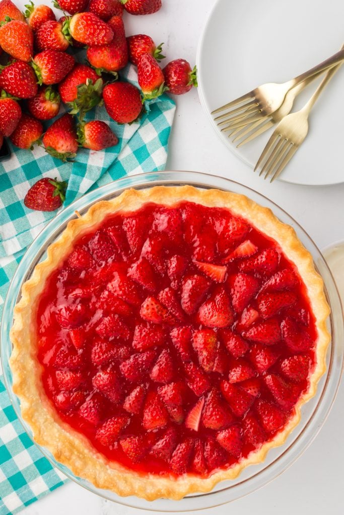 overhead shot of a fresh strawberry pie next to two gold forks.