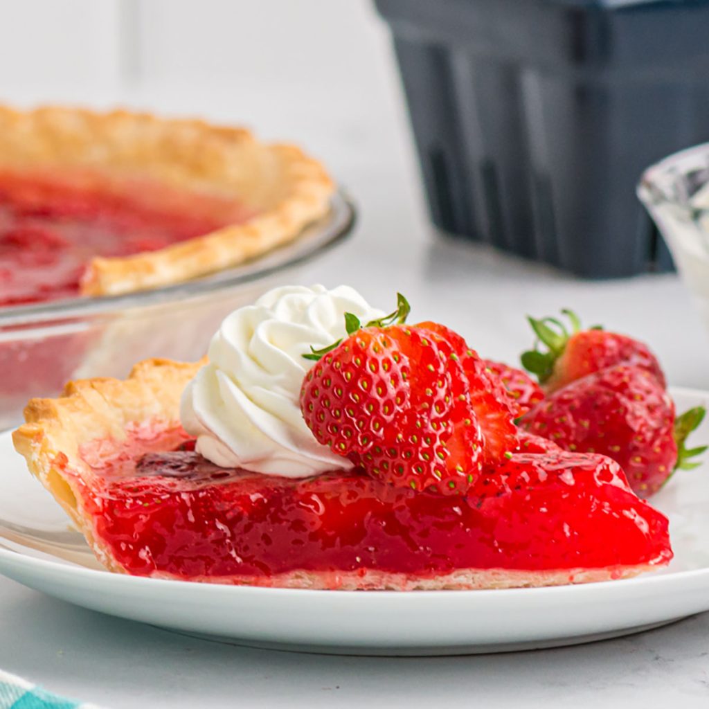 slice of fresh strawberry pie topped with whipped cream and a sliced strawberry.