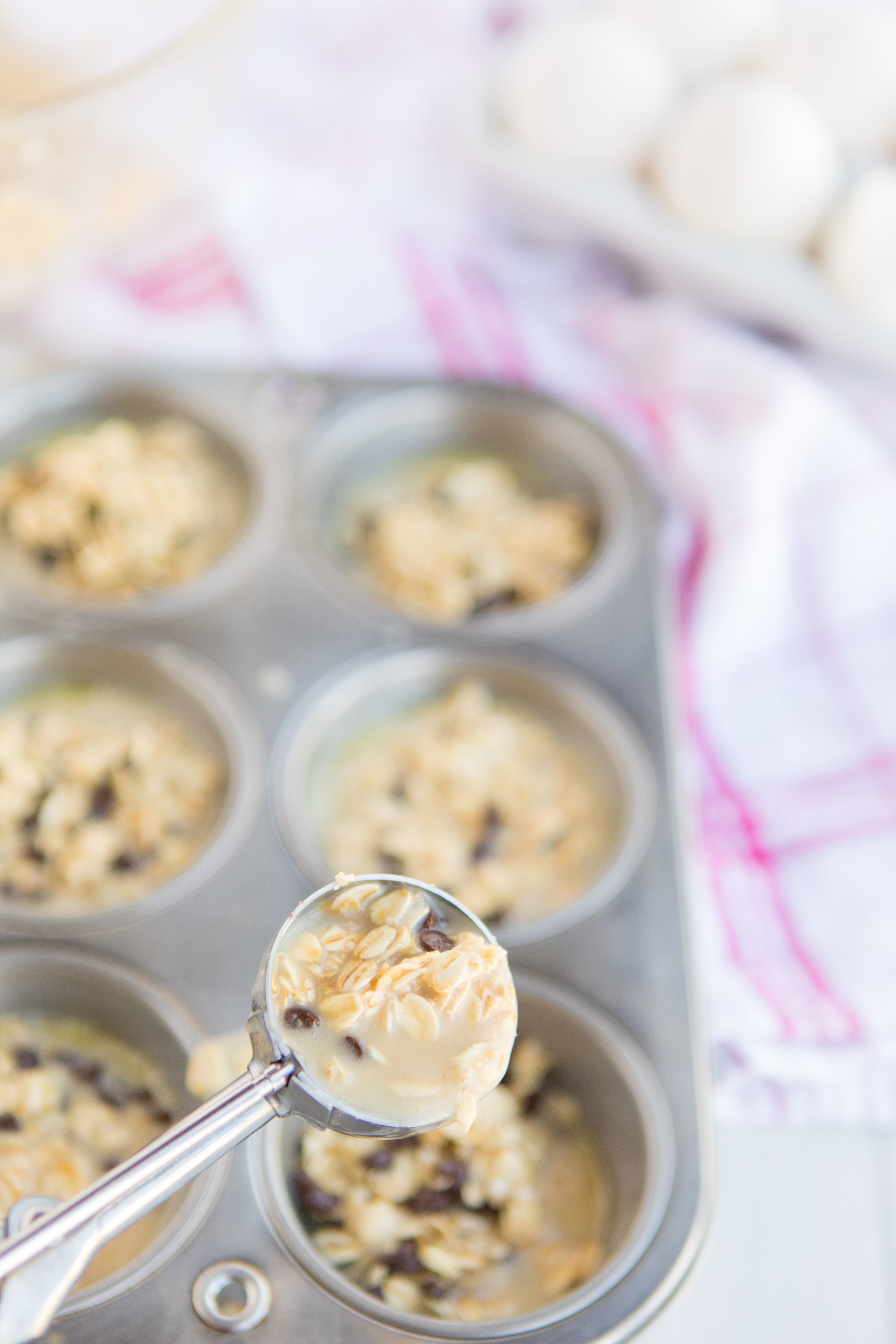 muffin pan of Baked Oatmeal Breakfast Cups with a cookie scoop portioning out batter