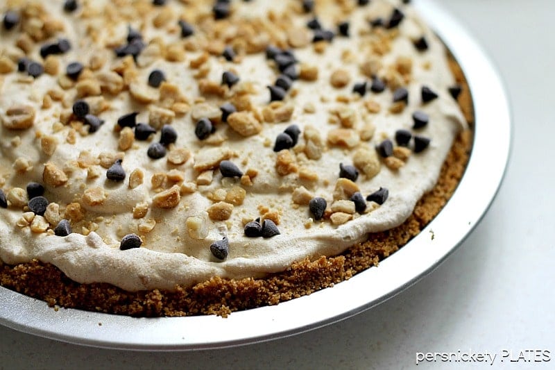peanut butter pie in a metal pie plate topped with crushed peanuts and mini chocolate chips.