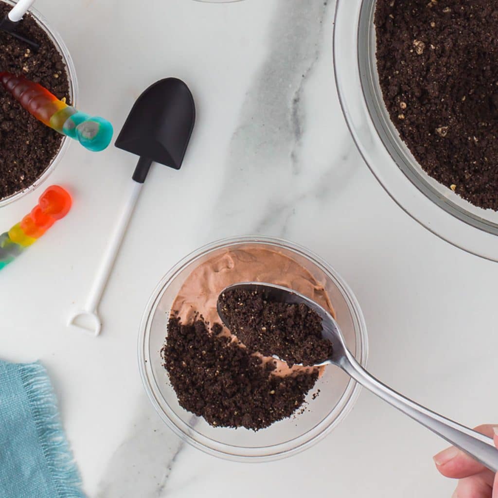 spoon layering oreo crumbs onto chocolate pudding in a cup.