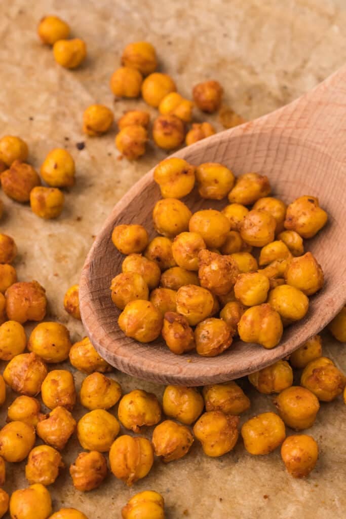 wooden spoon scooping roasted chickpeas from a cookie sheet.