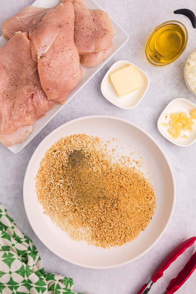 seasoned breadcrumbs on a plate next to chicken breasts.