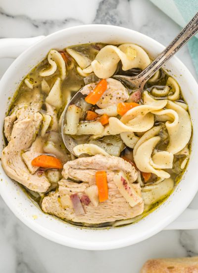white bowl of chicken noodle soup with a spoon in it