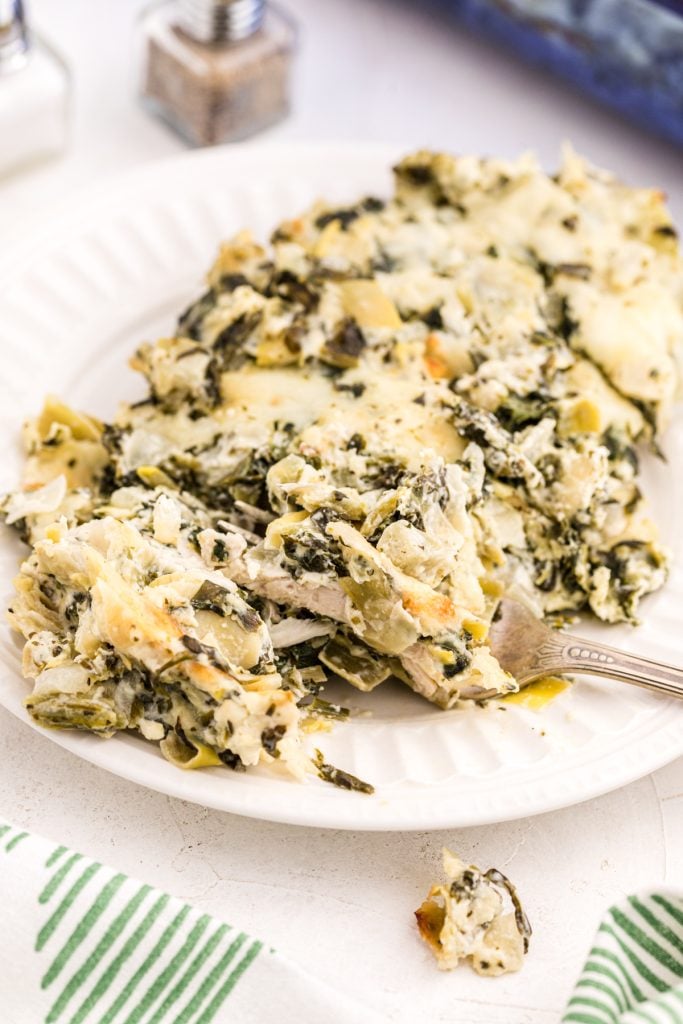 spinach artichoke chicken casserole on a white plate with a fork in it.
