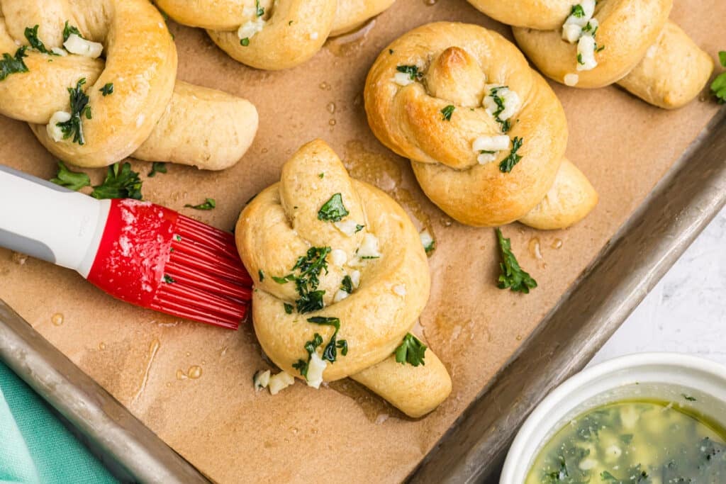 garlic knots being brushed with garlic butter.