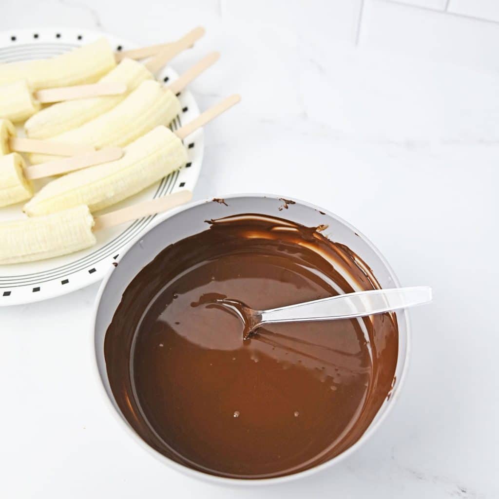 bowl of melted chocolate next to a plate of bananas.