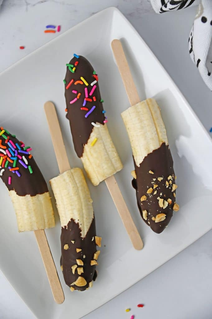 plate of frozen chocolate covered bananas topped with sprinkles.
