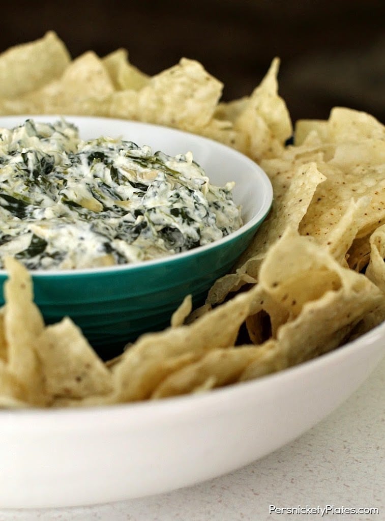 closeup of a bowl of spinach artichoke dip surrounded by tortilla chips