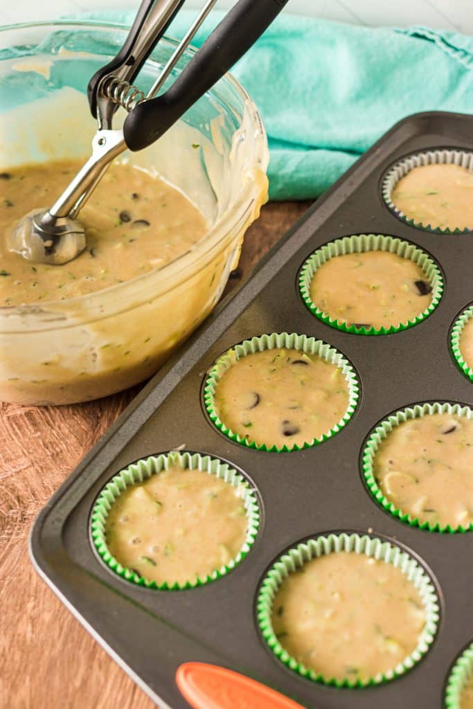 muffin pan next to a bowl of batter with a cookie scoop.