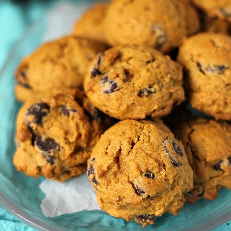 Close up of a platter of pumpkin chocolate chip cookies on a clear plate and a teal napkin